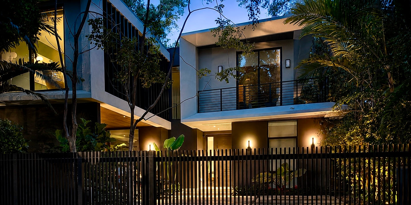 Casa moderna al anochecer detrás de una reja negra de listones verticales, con la fachada iluminada